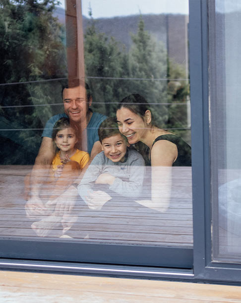 Family of four relaxing behind the large glass panel of an Imperial sliding patio door in a Calgary home, highlighting clear views and energy-efficient comfort by Glarior.
